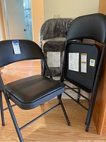 View of three folding chairs, one open, two folded, showing vinyl padded seats and backs with metal frames.