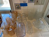 Overview of pitcher, six small amber glasses, two plastic butter dishes, clear bowls, clear rectangular divided dish, and a glass ring.