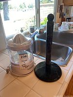 Juicer and marble paper towel holder together on countertop near sink.