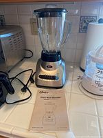 Full image of Oster blender with glass pitcher and user manual on countertop