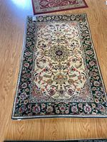 Full view of a 5x3 silk Persian style rug on wood floor showing overall pattern and border design.