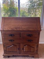 Front view of closed secretary desk showing two top drawers with decorative metal handles above two paneled cabinet doors