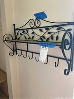 Metal decorative wall shelf featuring a leaf design, wooden shelf, and hooks beneath