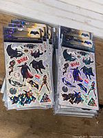 Stacked packs of holographic superhero sticker sheets featuring Batman, Superman, Wonder Woman