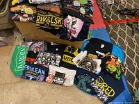 View of folded pile of assorted men's XL T-shirts showing a variety of nerdy themes including anime characters, cartoon faces, and text logos.