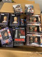 Box filled with various boxed action figures including Buffy the Vampire Slayer, Last of Us, Predator, Assassin's Creed, and Sherlock Holmes.