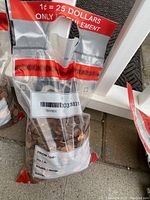 Clear plastic bag containing approximately 2,500 used pennies. Bag is marked with red and white label stating value equivalency and other printed information.
