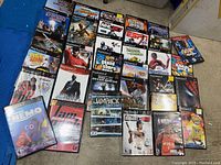 Image of 25 original PlayStation 2 game cases laid out on floor. Clean cases with minor wear visible. Titles and cover art visible.