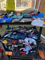 Photo of folded colorful T-shirts laid out on a black metal rack, showing various graphic designs including Marvel and cartoon themes.
