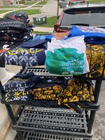 Multiple stacks of folded new 2XL t-shirts with various graphics and colors, shown on a black plastic shelf outdoors.