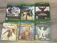 Photo showing 6 Xbox One game cases arranged 2 rows of 3 each. The bottom three are new sealed and the top three are in used condition.