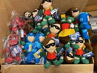 Box containing a variety of plush toys including Robin and Deadpool characters, some still in plastic packaging.