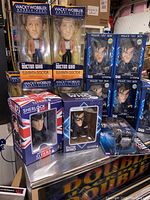 Boxed Doctor Who bobblehead and figurine toys from multiple angles showing Eleventh Doctor and Tenth Doctor bobbleheads plus Sherlock Holmes figure