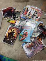 Comic books spread out on floor showing various titles including Red Sonja, Aliens, and superhero comics. Most are in protective plastic bags and backing boards.