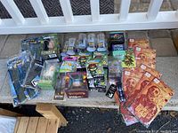 Full overview of all items in the lot laid on concrete steps including multiple packaged figures, trading card packs, puzzle cubes, and posters.