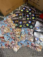 Photo showing multiple pinback buttons spread out on floor. Included are Sonic the Hedgehog character pins on Sega Genesis branded cardbacks and other pins featuring video game or comic characters on different cardbacks.
