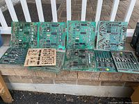 Full overview of eleven vintage pinball circuit boards laid out in two rows outdoors, showing various components and overall condition.