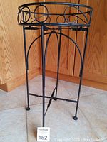 Front view of tall black metal plant stand with decorative open frame and circular patterns at upper rim.
