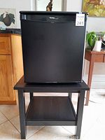 Front view of the black Danby portable bar fridge on top of the black IKEA table