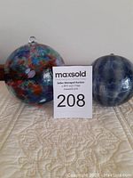 Two friendship glass balls displayed side by side, one multi-color and one smoky blue, showing size difference and condition.