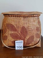 Front view of birch bark basket showing floral leaf designs, leather strap, and sewn edges