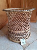 Front view of large hourglass-shaped rattan plant holder showing natural twisted woven pattern and reinforced top rim.
