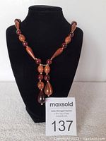 Front view of vintage wooden bead necklace on black display stand with auction card