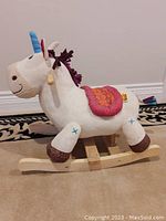 Side view of white plush rocking horse with maple wood rocking base on carpet.