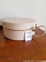 Closed oval travel makeup sample case with cream-colored faux ostrich vinyl exterior and a side handle