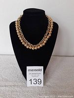Front view of the vintage gold coloured two strand necklace displayed on a black velvet jewelry stand, showing round beads and chain detail.