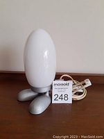 Front view of vintage IKEA Dino Egg table lamp with white egg-shaped glass shade on silver feet base, electrical cord visible.