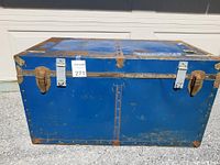 Front view of the vintage blue metal steam trunk showing metal latches, corner protectors, and overall wear.