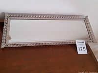 Full frontal view of the vintage rectangular vanity mirror showing the ornate metal filigree border in an off-white or silver-tone.