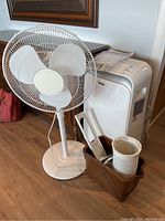 Front view of white oscillating stand fan and portable air conditioner with accessories on floor