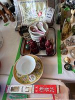 Photo showing ceramic bowls, plates, two red figurines, decorative fan, boxed chopsticks, and a green decorative ball.