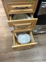 Open drawers showing various bakeware dishes and plates inside wooden drawers near stove.