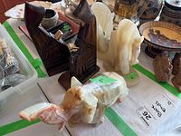 Photo showing dark wood carved abstract figure bookends, translucent stone horse bookends, and carved stone elephant on a table with various other items.