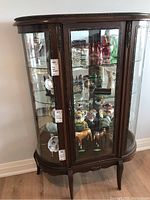 Front view of cabinet showing arched glass door, wood frame, interior display items and glass shelves