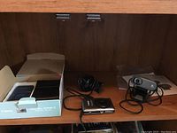 Shelf holding Canon PowerShot SD940 IS camera in the open box, Logitech webcam with USB cable, and other accessories.