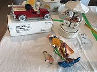 Photo showing the red 1926 Seagrave fire truck bank in its white box, ceramic carousel figurine with horse, and two plastic clown figurines scattered around the table.