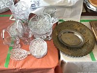 Overview of cut glass items and two metal plates on an orange surface. Includes baskets, bowls, and ashtrays visible.