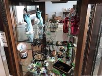 Full view of display cabinet showing Coalport figurines, art glass vases, and decorative floral pieces on glass shelves.