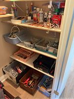 Overall view of three closet shelves with various hardware and homeware items stored in plastic bins, boxes, and loosely arranged on shelves.