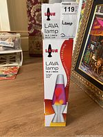 Photo of the lava lamp box standing upright on wooden floor, showing brand name and size 14.5 inch.
