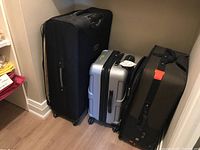 Three pieces of luggage standing upright showing black soft suitcase, silver hard suitcase, and brown soft suitcase