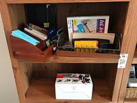 Wide photo showing two wooden shelves filled with various office supplies including wooden organizers, metal rack with ink cartridges, and a boxed slide film scanner on lower shelf.