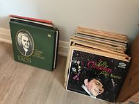 Two stacks of vintage vinyl records on the floor, one topped with "A Jolly Christmas from Frank Sinatra" and the other with "Great Men of Music Bach".