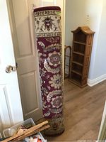 Rolled-up red and beige floral area rug showing overall design and border detail.