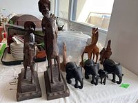 Group of wooden carved figures including two people on horses, three giraffes in background, and four elephants.