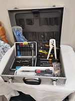 Full open aluminum case with tools arranged inside showing screwdrivers, wire strippers, crimper, pliers, and soldering set box.